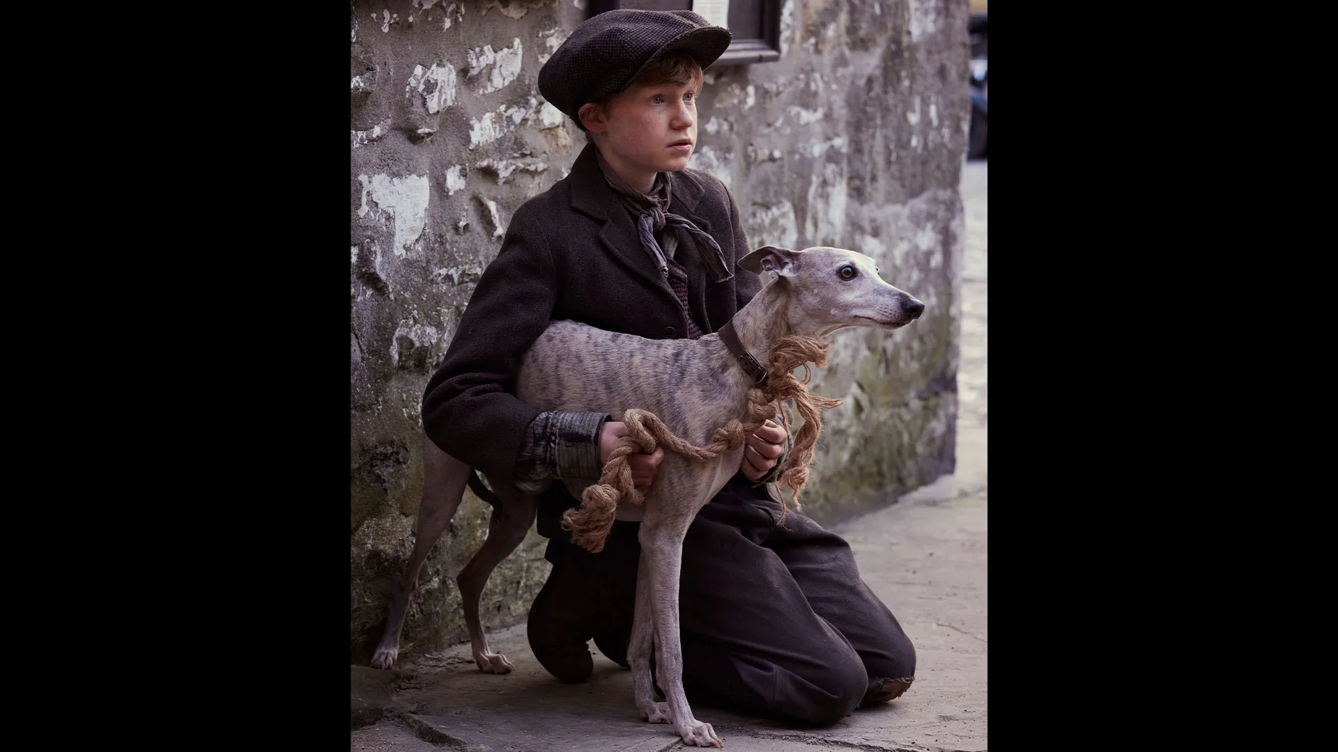 Crouched down, the boy Wesley Binks olds his frightened-looking whippet, Duke.