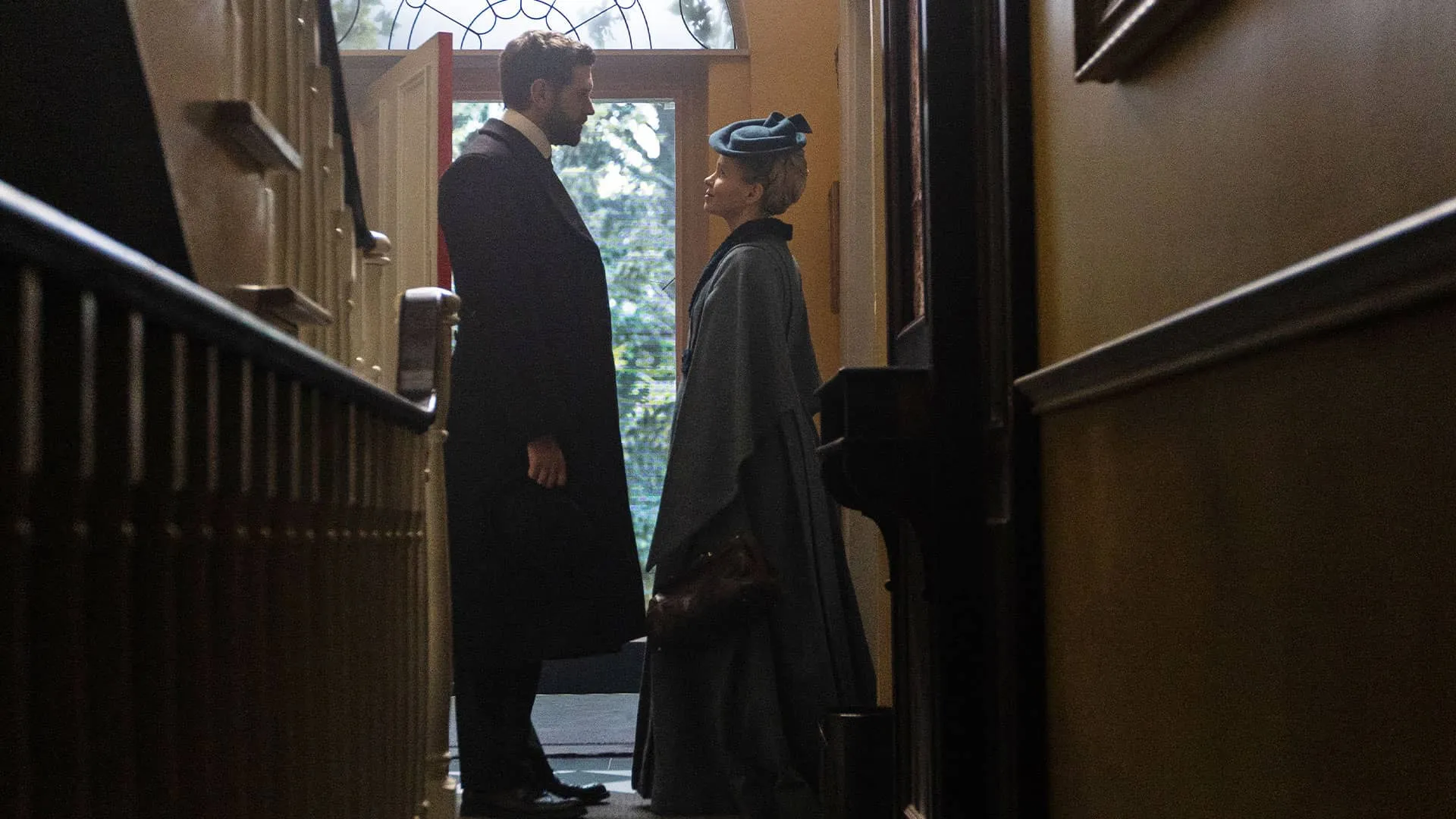 A man and woman in Victorian-era dress stand facing each other in a doorway.